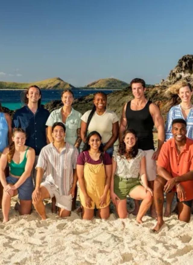 Survivor cast poses on beach with ocean, cliffs, and islands.