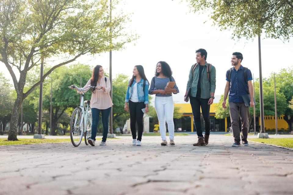 A group of student friends walking together after class carrying books and laptops.